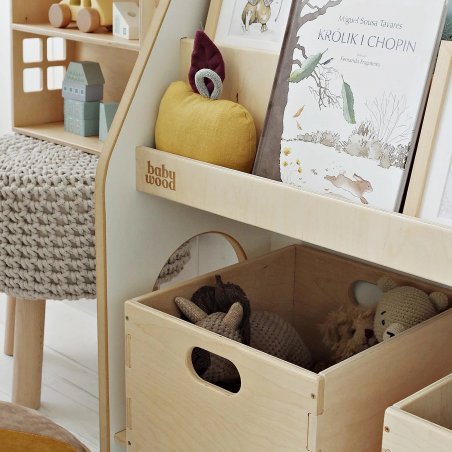 Nahaufnahme eines Kinderregals aus Holz mit abgerundeten Kanten, Büchern und Spielzeugkiste