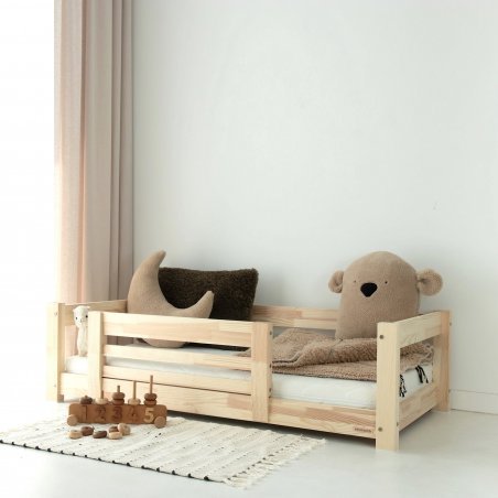 Holzbett mit einfacher vorderer Schutzbarriere, auf dem Bett Stofftiere und Decke Holzbett mit einfacher vorderer Schutzbarriere, auf dem Bett Stofftiere und Decke