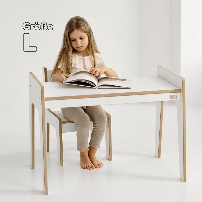 Weißer Kindertisch mit Stuhl, Mädchen sitzt und blättert in einem Buch.