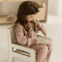 Mädchen sitzt auf weißem Stuhl, hält Montessori-Spielzeug im Kinderzimmer.